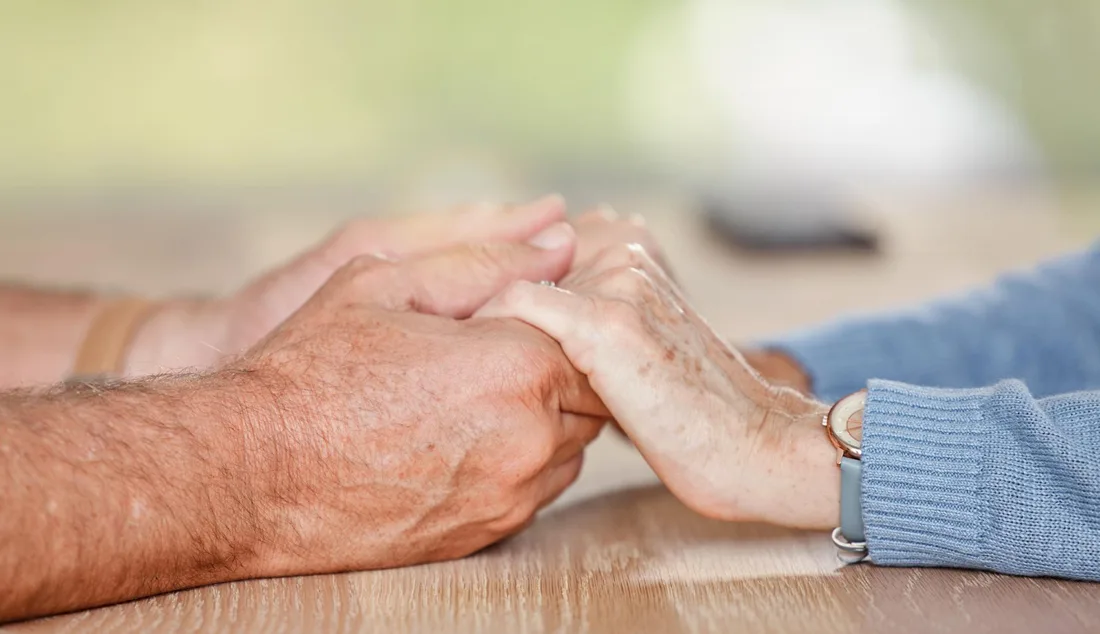 Person holding the hands of an older adult living with dementia