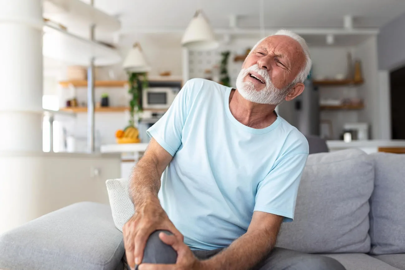 Older man experiencing chronic knee pain while sitting at home