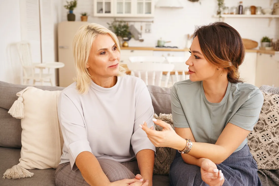 Younger woman supporting an older woman during a thoughtful conversation at home