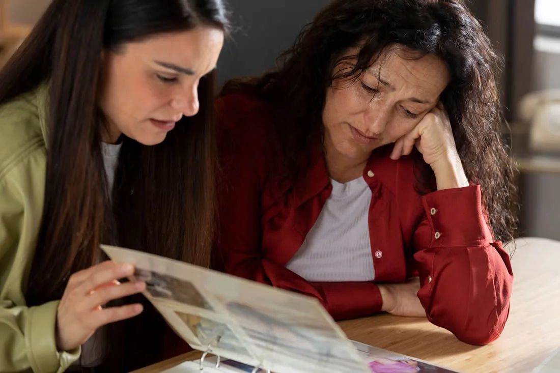 Two women looking through a family photo album while grieving a loved one.