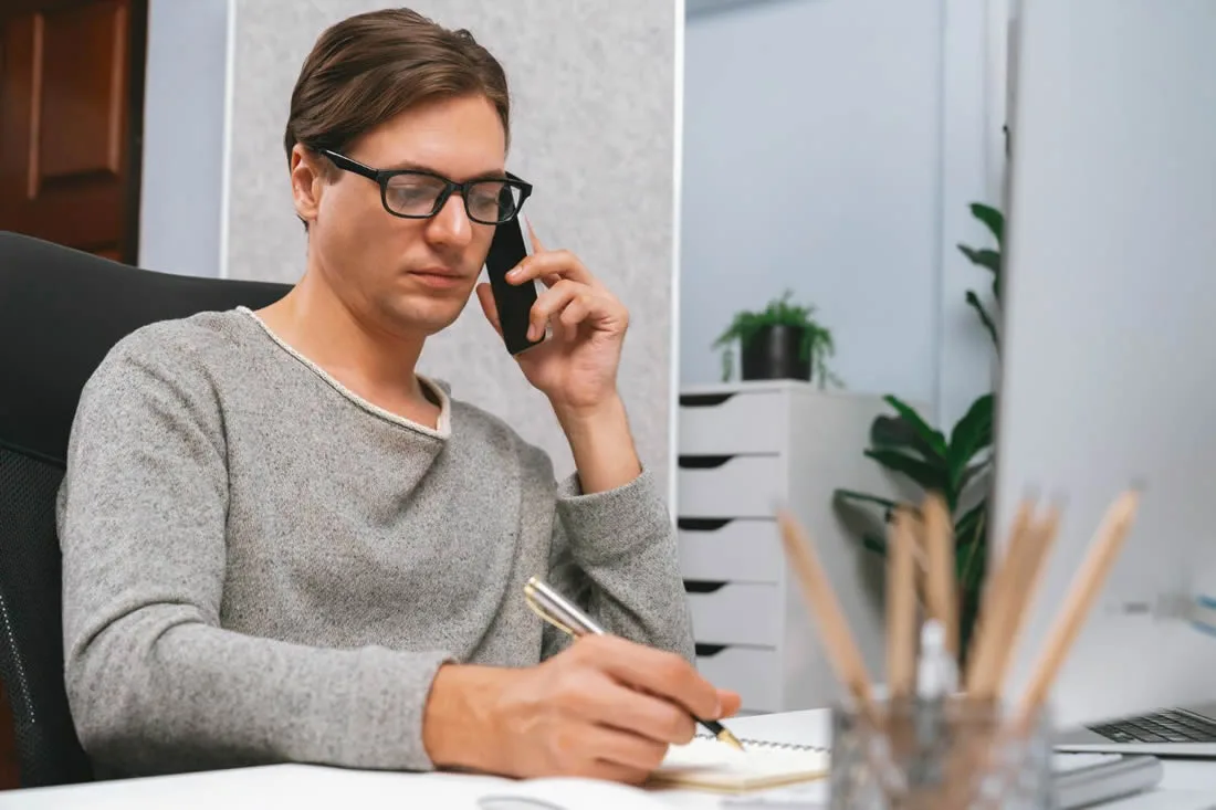 Man making phone calls and taking notes while managing practical affairs after a death.