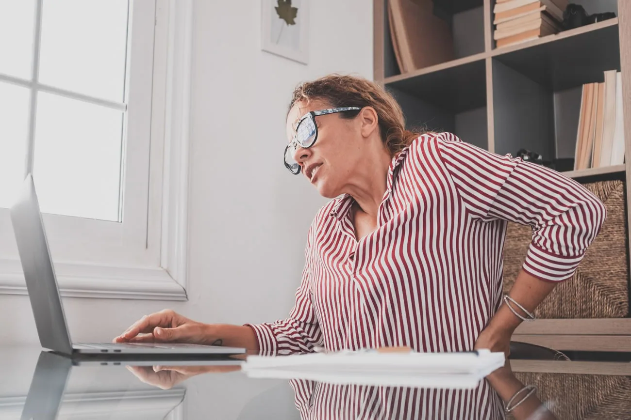 Woman experiencing back pain while working on a laptop at home