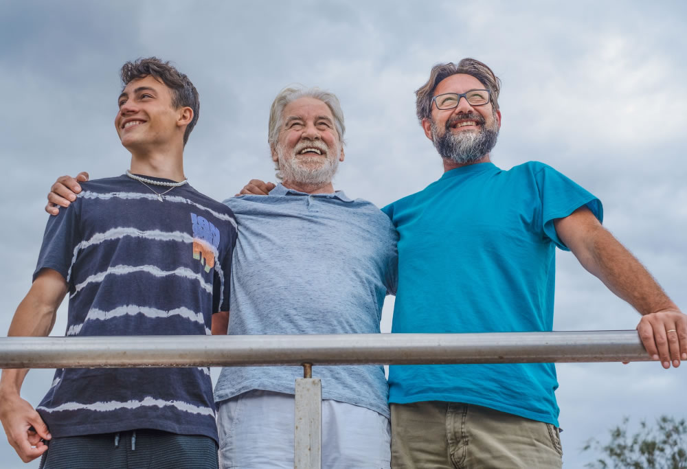 Three generations of men standing together outdoors with arms around each other.