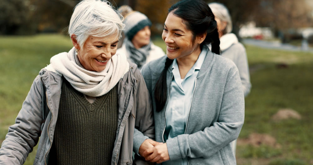 A carer walking alongside and supporting an older woman.