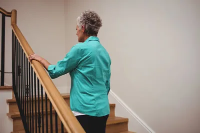 Older woman walking up stairs holding on to handrail