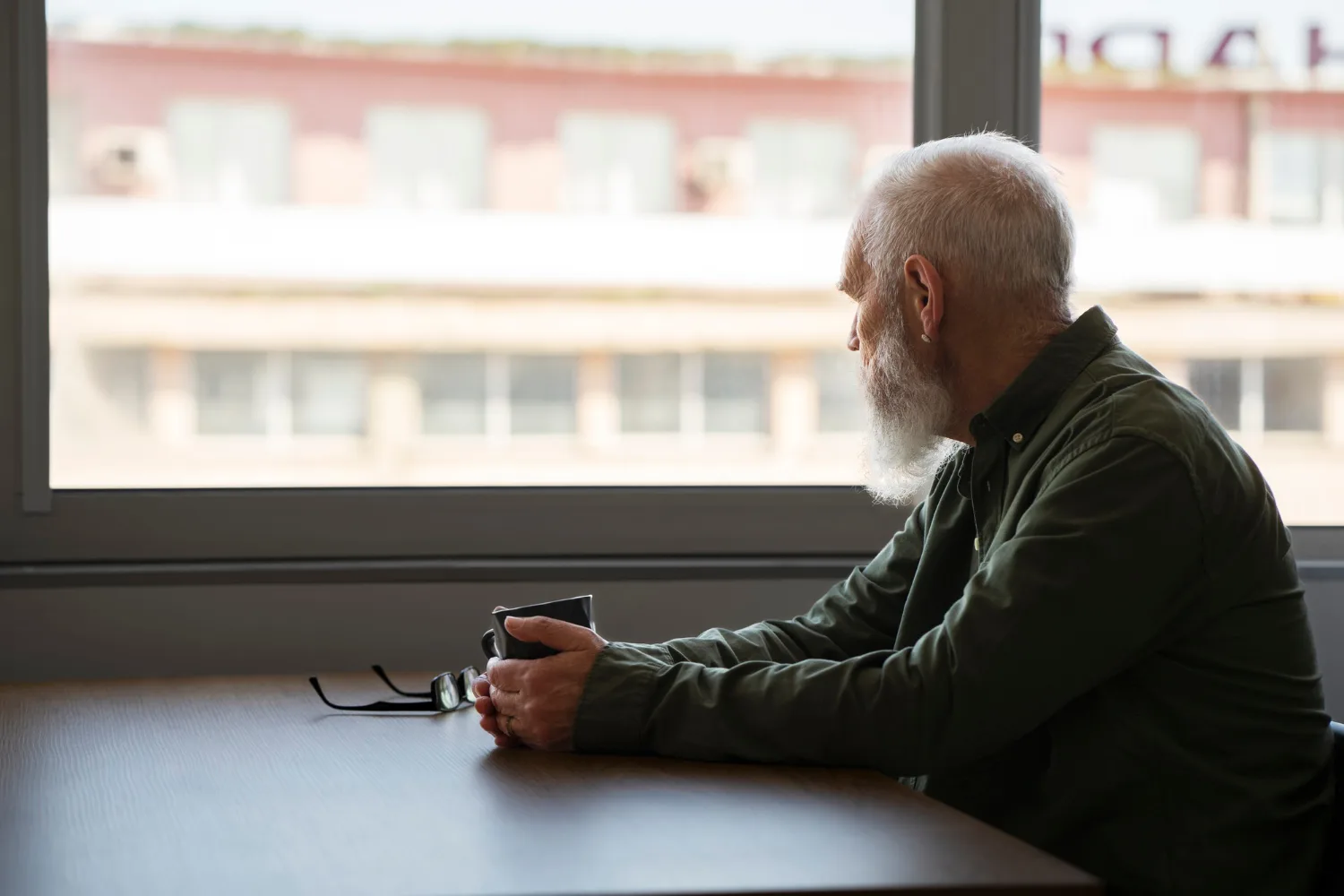 Older man sitting quietly by a window while experiencing the effects of grief