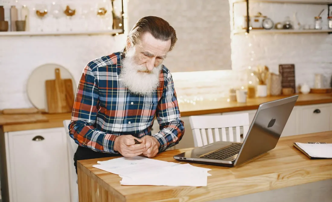 Older man reviewing paperwork and digital information after the death of a loved one.