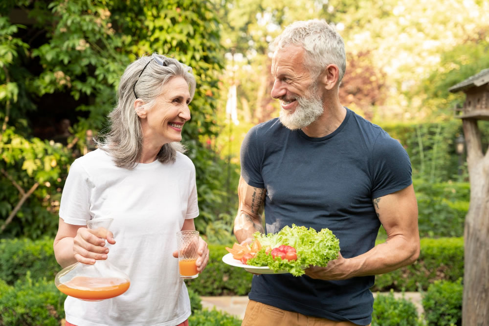 Older couple smiling while holding fresh food outdoors, representing heart-healthy living on World Heart Day.